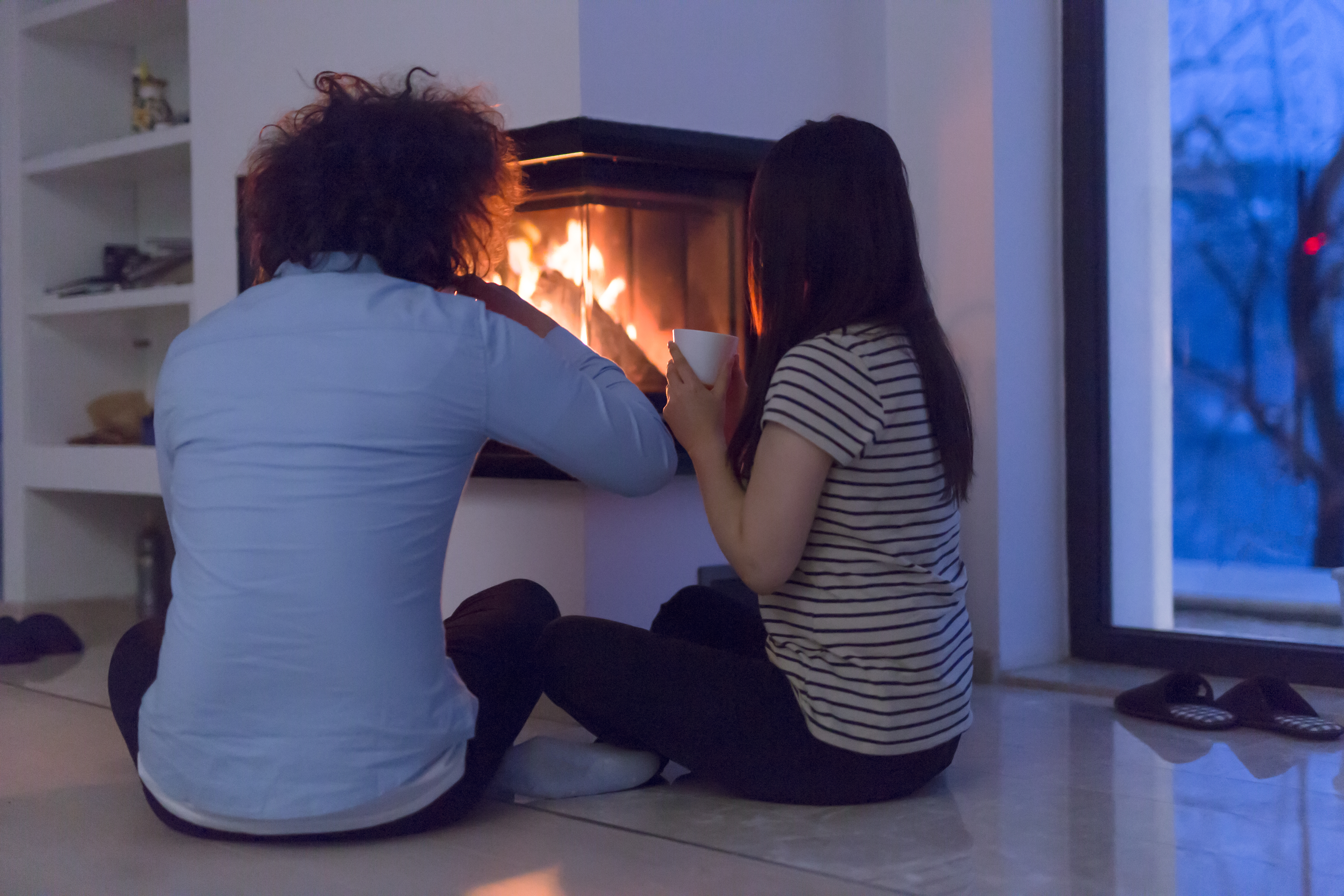 happy multiethnic couple sitting in front of fireplace